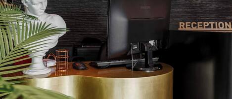 A reception desk with a gold finish, a white bust sculpture, and a reception sign.