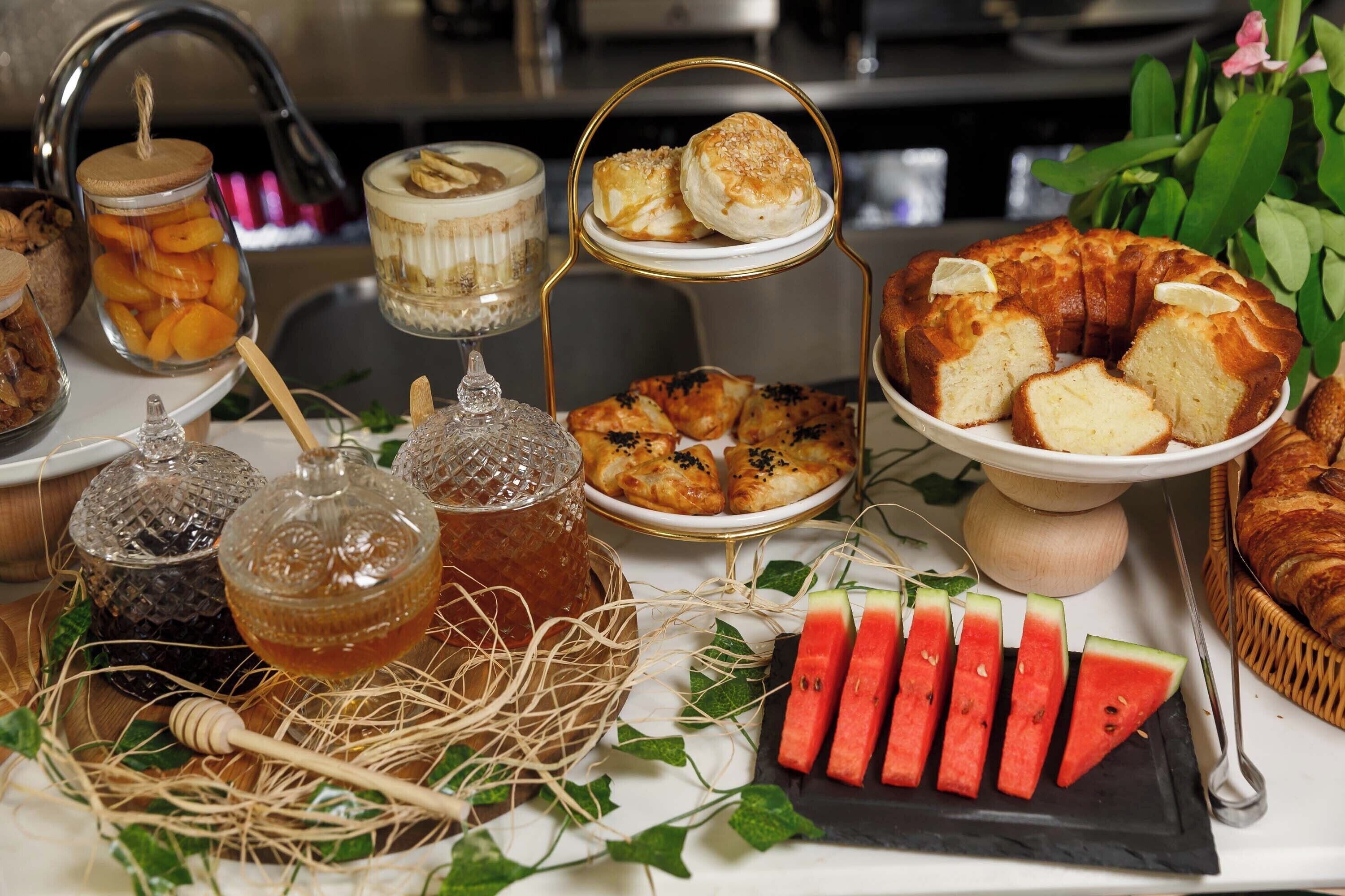Una mesa de buffet con diversos alimentos, como pasteles, un pastel y sandía en rodajas.