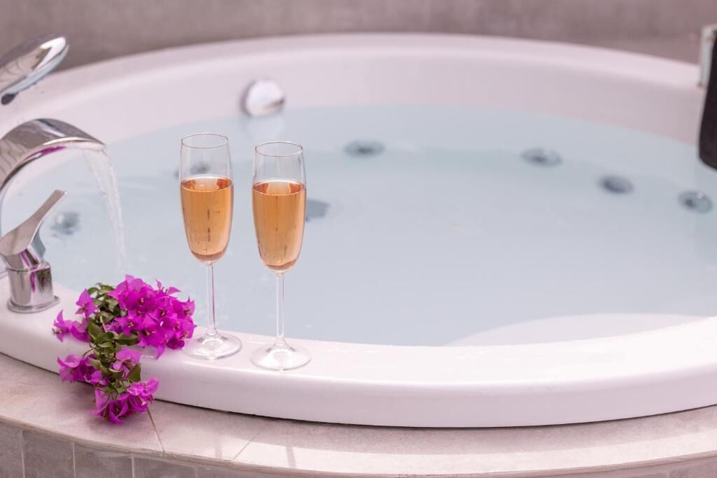 A bathtub with two champagne glasses and a bouquet of flowers.