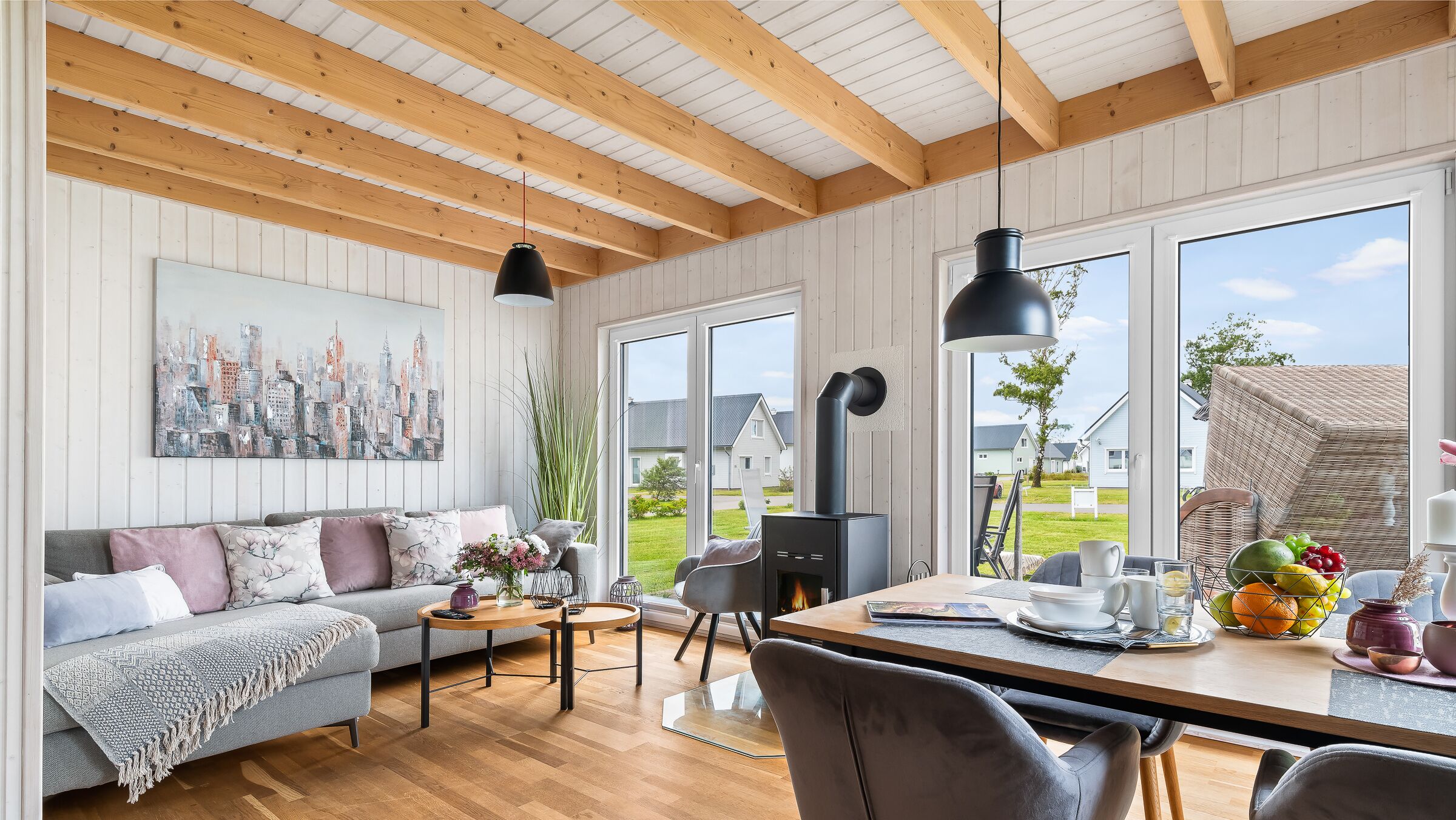A modern living room with a sofa, coffee table, and dining table. There is a fireplace, large windows, and a cityscape painting on the wall.