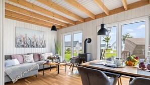 En moderne stue med sofa, sofabord og spisebord. Der er en pejs, store vinduer og et bybillede på væggen.