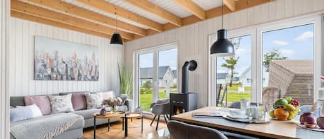 Ein modernes Wohnzimmer mit Sofa, Couchtisch und Esstisch. Ein Kamin, große Fenster und ein Stadtbild an der Wand sind ebenfalls vorhanden.