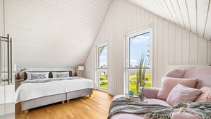 Et soveværelse med seng, sofa og store vinduer med udsigt over det fri.