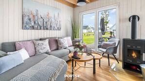 En moderne stue med en grå sofa, et rundt træsofabord, en sort pejs og et bybillede på væggen.