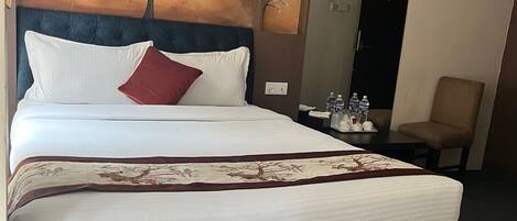 A hotel room with a large bed, a headboard with a tree painting, a small table with water bottles, and a chair.
