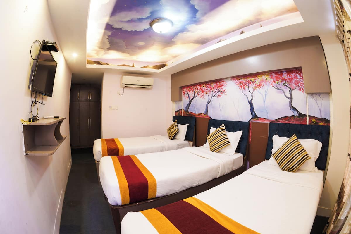 Quarto de hotel com três camas de solteiro, TV fixada na parede, um mural no teto e aparelho de ar condicionado.