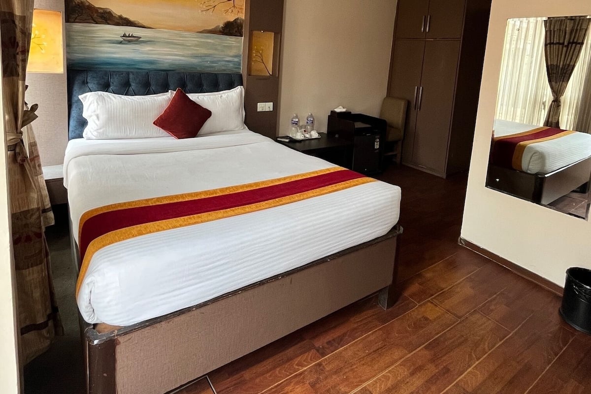 Quarto de hotel com cama grande, pintura de paisagem, escrivaninha com cadeira e guarda-roupa.