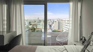 A bedroom with a large window, a bed, a chair, and a small table. -  Limassol Seaside Residences 06 (Limassol)