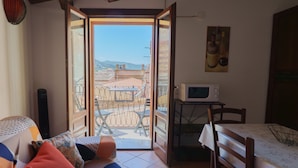 A cozy room with a sofa, a dining table with chairs, a microwave, and a view of the outside. - La Casa del Bastione a Cefal by Wonderful Italy (Cefalù)
