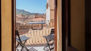 A balcony with metal chairs and a table, overlooking a courtyard with buildings and a clear sky. - La Casa del Bastione a Cefal by Wonderful Italy (Cefalù)