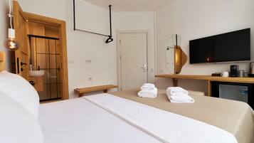 A hotel room with a bed, a wooden door, a TV, and a desk with a mirror.