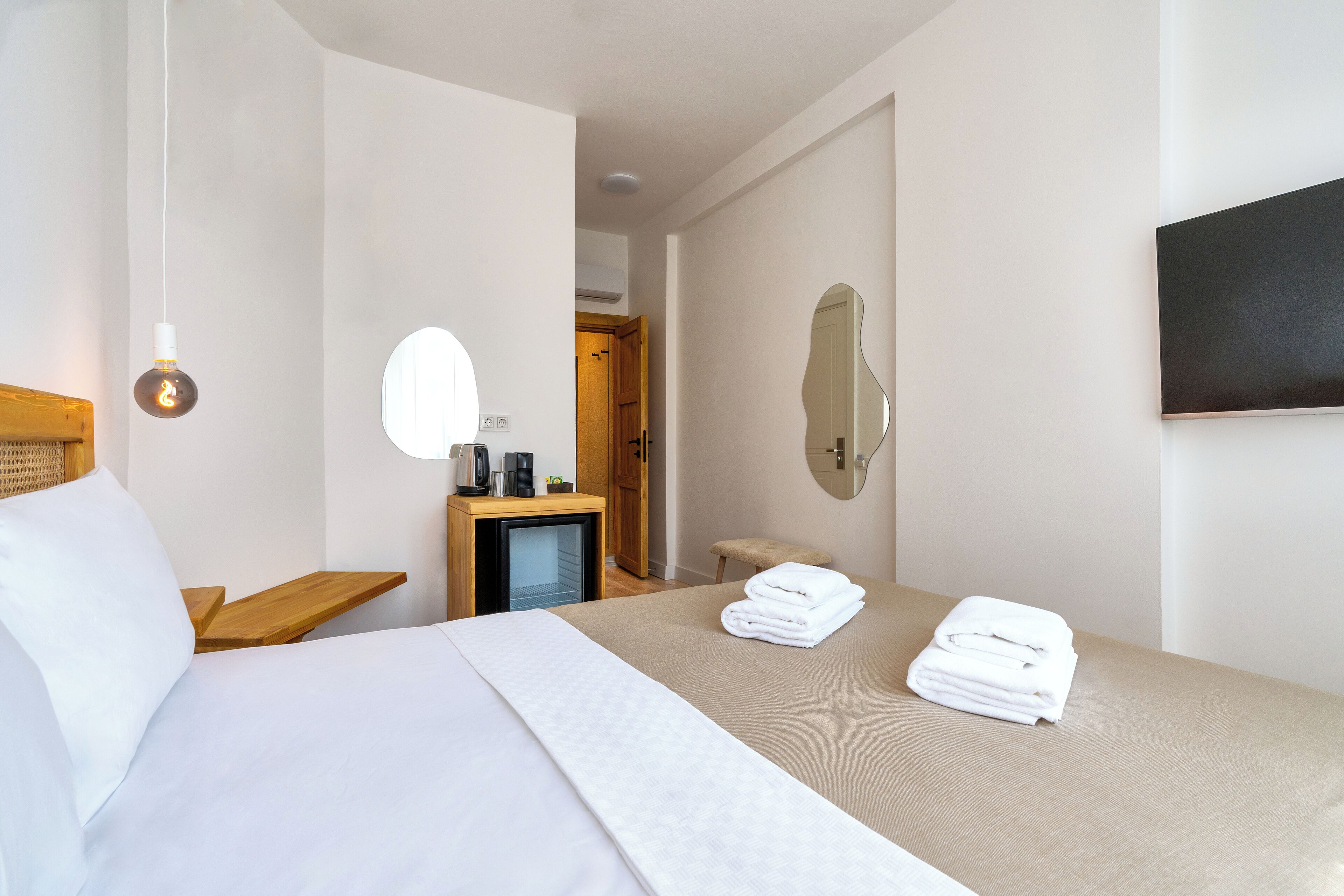 Habitación de hotel con cama, mesita de noche con lámpara, televisor y espejo en la pared.