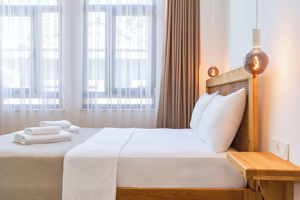 A hotel room with two beds, a wooden headboard, a bedside table, and a lamp.