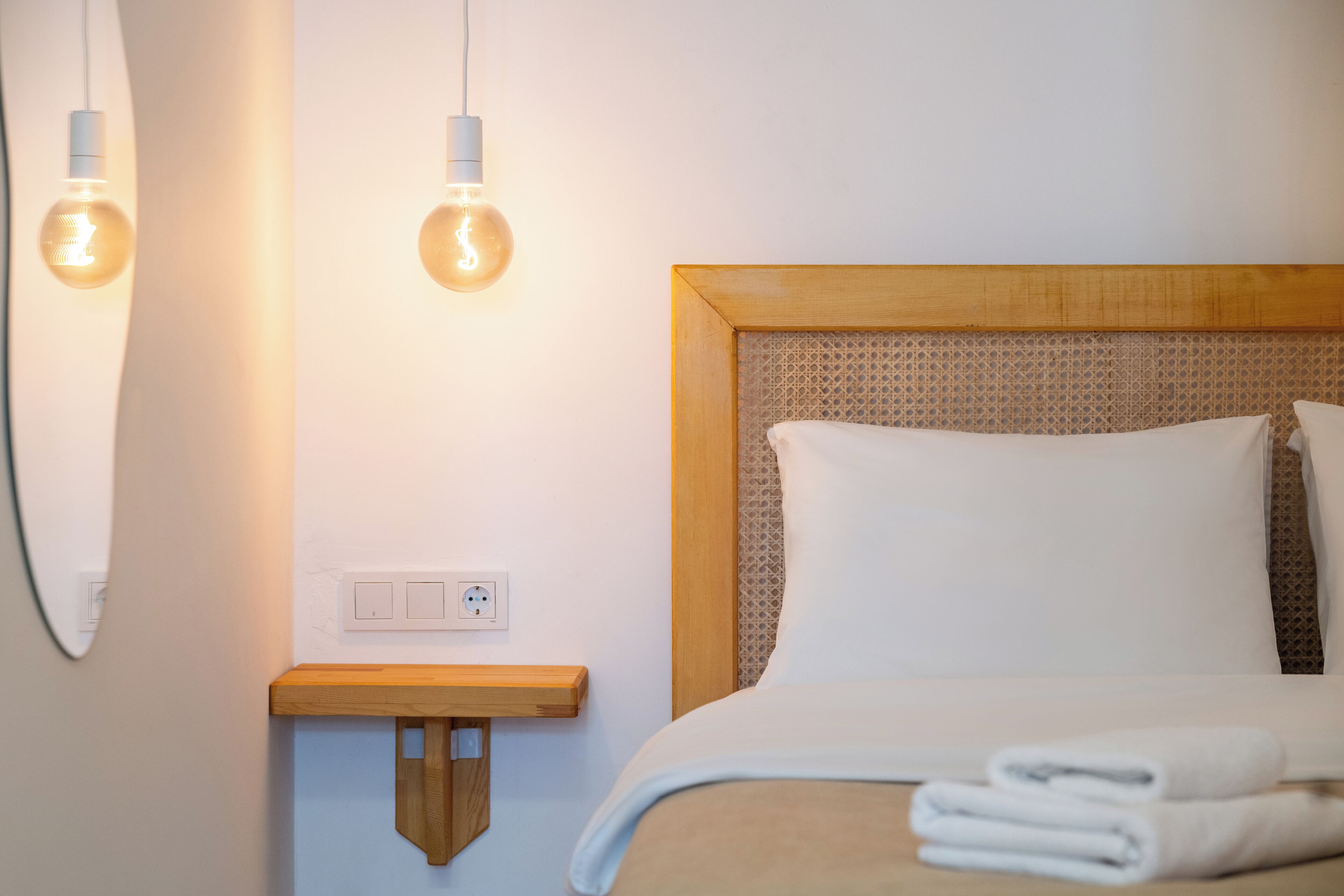 Une chambre d’hôtel avec une tête de lit en bois, une table de chevet et deux appliques murales.