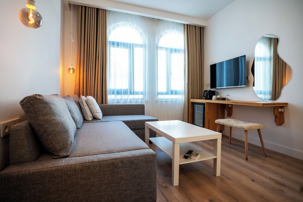 A modern living room with a sectional sofa, a white coffee table, a small wooden desk with a TV, and a large mirror.