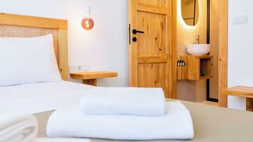 Een keurig opgemaakt bed met witte lakens, een houten deur met een spiegel en een klein houten nachtkastje met een lamp.