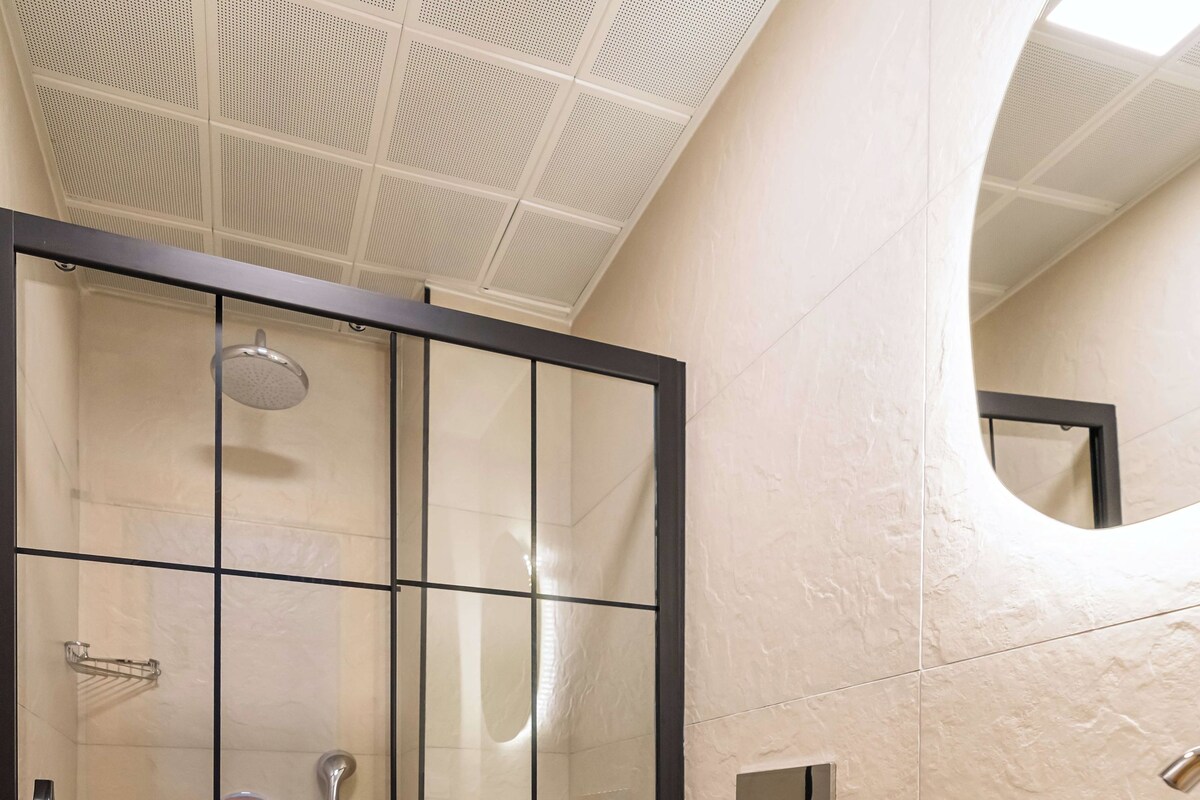 A modern bathroom with a glass-enclosed shower, a white toilet, and a wooden vanity with a round sink.