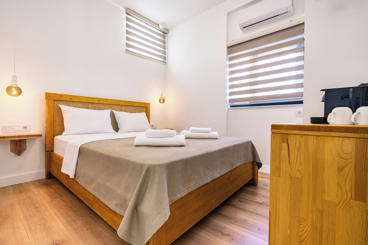 A neatly made bed with white linens and a wooden headboard, a bedside table with a lamp, and a wooden dresser.