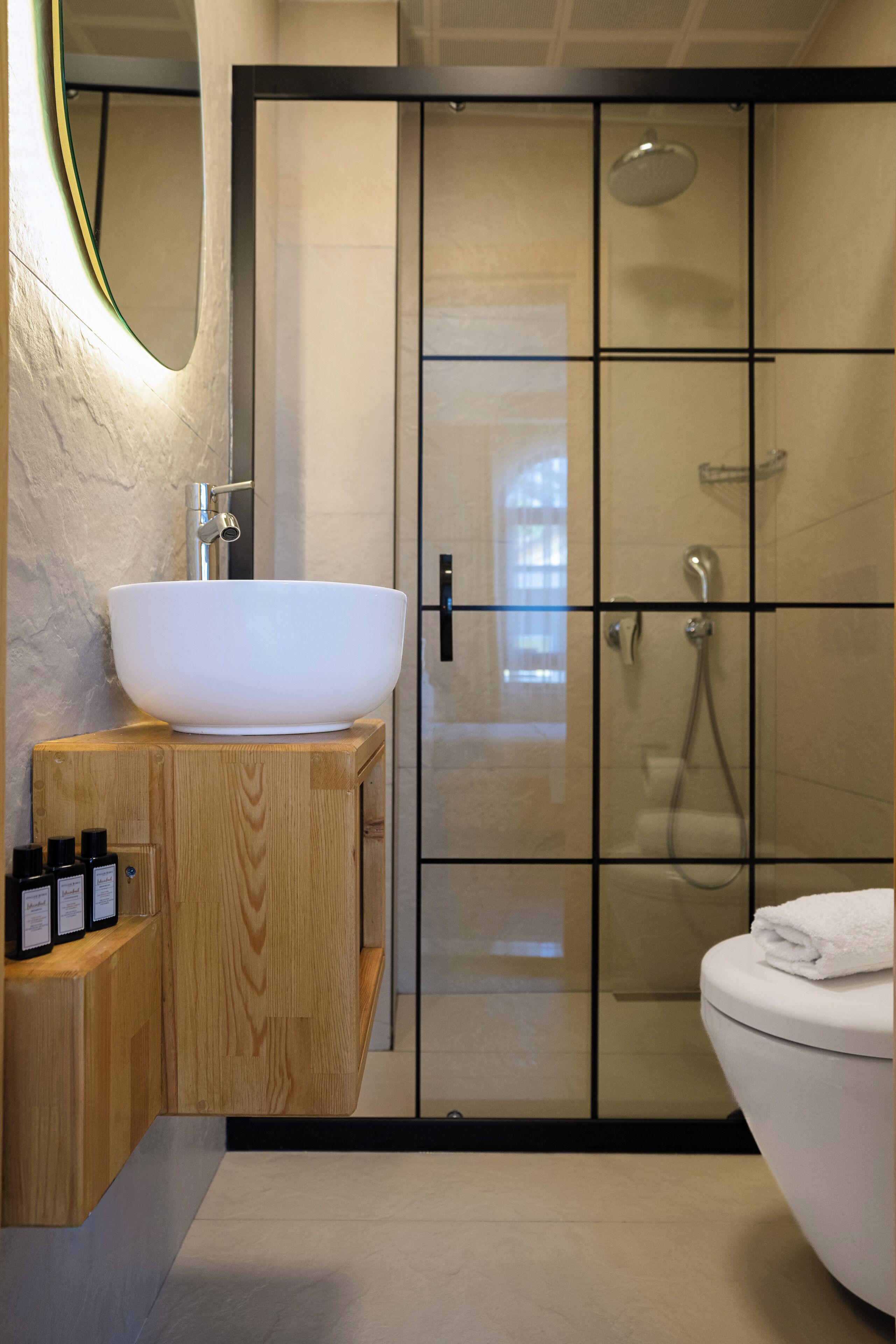 A modern bathroom with a large white vessel sink, wooden vanity, and a glass-enclosed shower area.