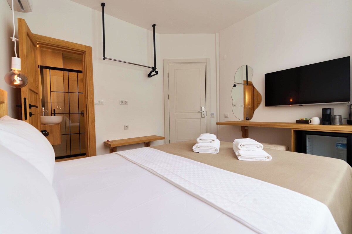 A hotel room with a bed, a wooden door, a television, a desk, and a small refrigerator.