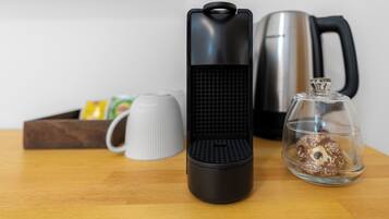 A kitchen area with a coffee maker, a kettle, a mug, and a glass container with a donut.