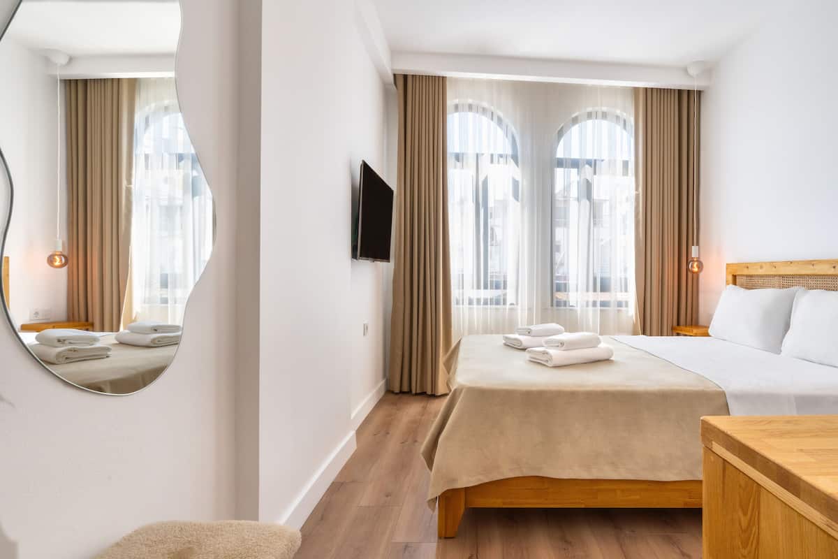 A hotel room with a bed, a bedside table, a TV mounted on the wall, and a large mirror.