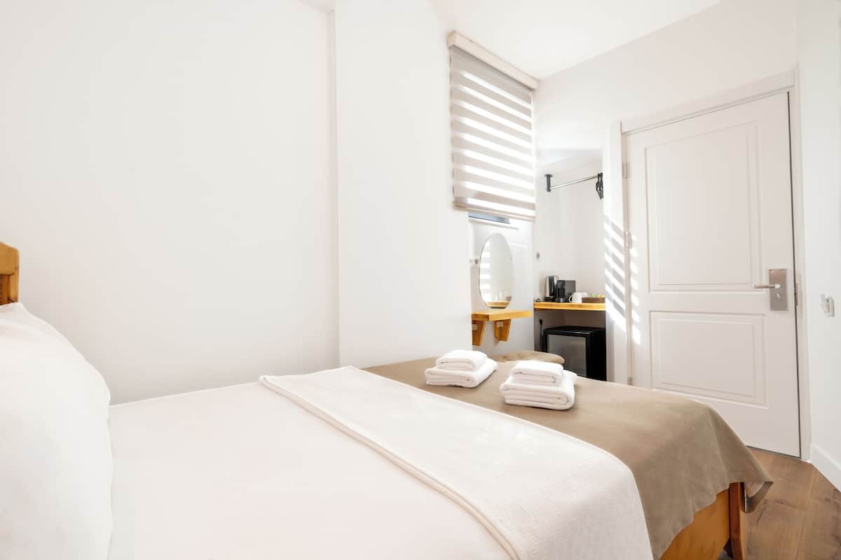 A neatly arranged bedroom with a bed, a bedside table, a mirror, and a door.