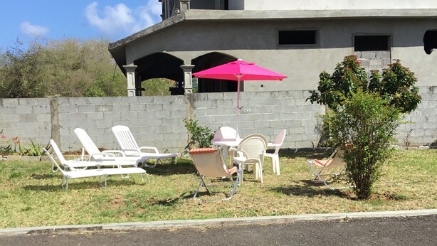 A building under construction with a patio area featuring white lounge chairs and a pink umbrella. - Appartement privatif ou location de chambres - Villa Lotus Paradise (Calodyne)