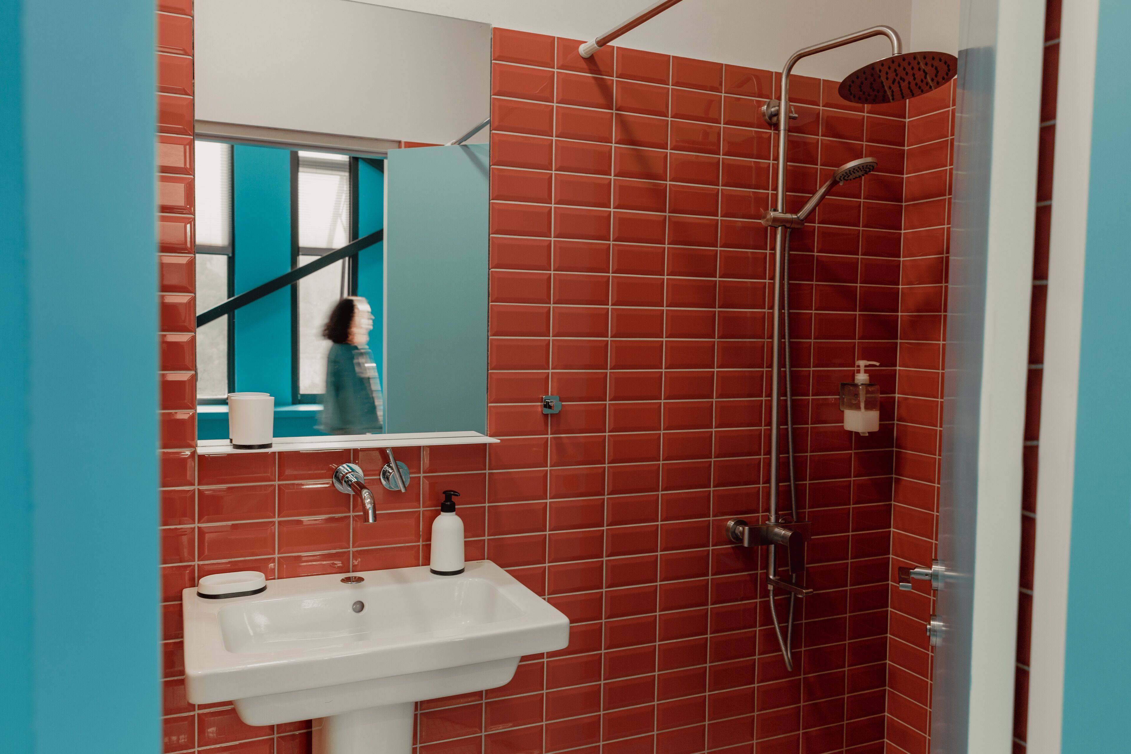 A bathroom with a white sink, a mirror, and a shower with red tiles.