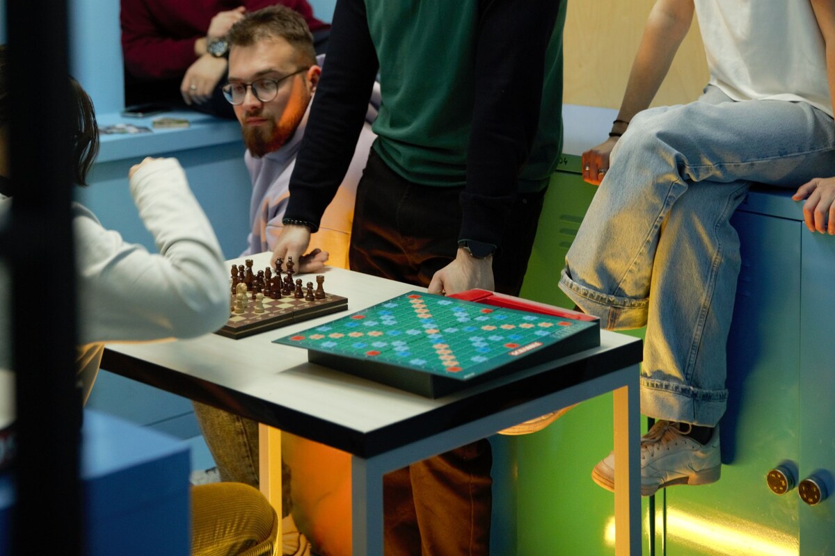 A group of people playing chess in a room with a wooden wall and a window.