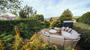 Ein Garten mit Korbmöbeln, darunter eine Couch und runde Tische.