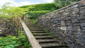 Eine Steintreppe mit Holzgeländer, umgeben von viel Grün.