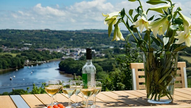 A table with a bottle of wine, glasses, and a plate of tomatoes, overlooking a river with boats. - Morawel, St Dogmaels (Saint Dogmaels)