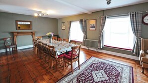 A dining room with a wooden table, chairs, a vase of flowers, a fireplace, and a large window with curtains. - Mount Pleasant, Newport (Newport)