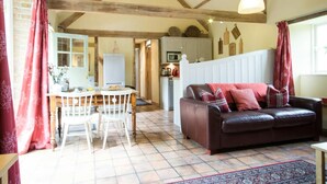 A cozy living room with a brown leather sofa, a dining table with chairs, and a kitchen in the background. - Cinnamon Cottage, Newcastle Emlyn (Felindre)