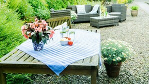 A garden patio with a table set for two, surrounded by wicker furniture and potted plants. - Cinnamon Cottage, Newcastle Emlyn (Felindre)