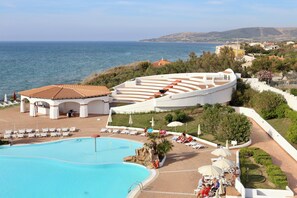 Un resort con una amplia piscina, mobiliario exterior y vistas al mar.