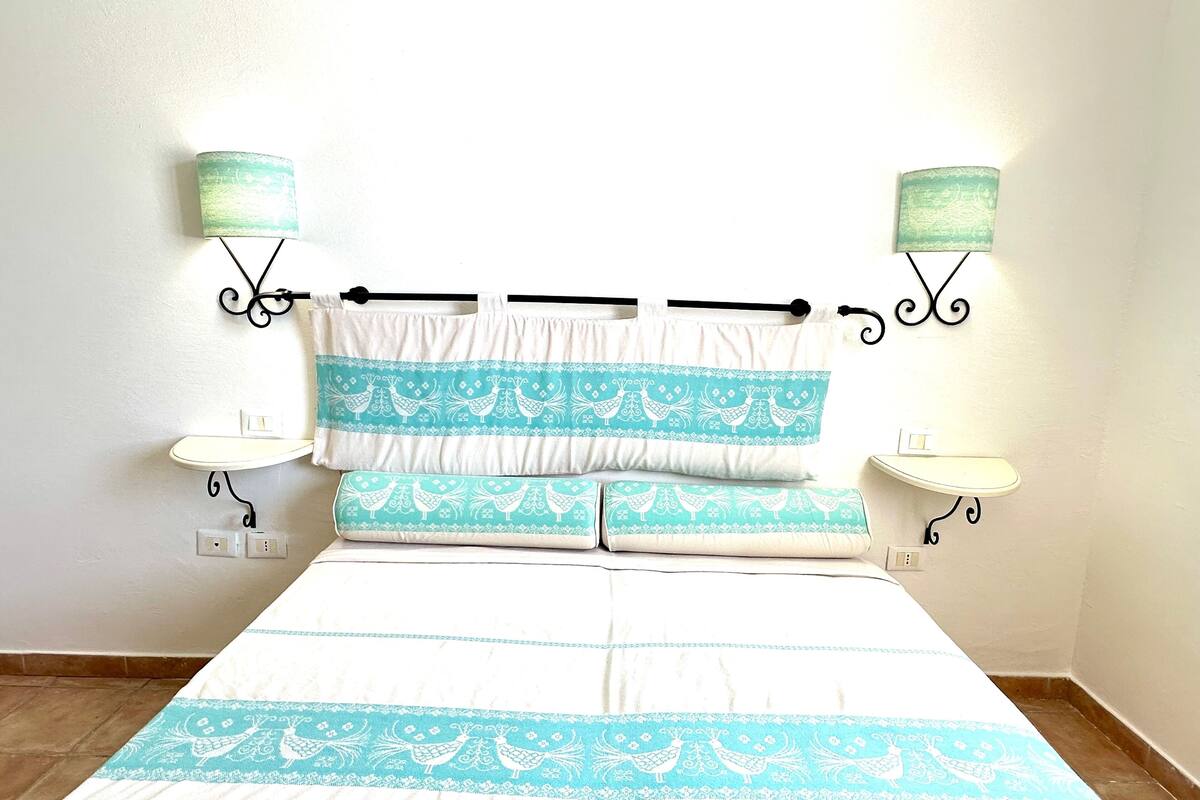 A bed with a white and blue patterned bedspread, two matching pillows, and two bedside tables with lamps.