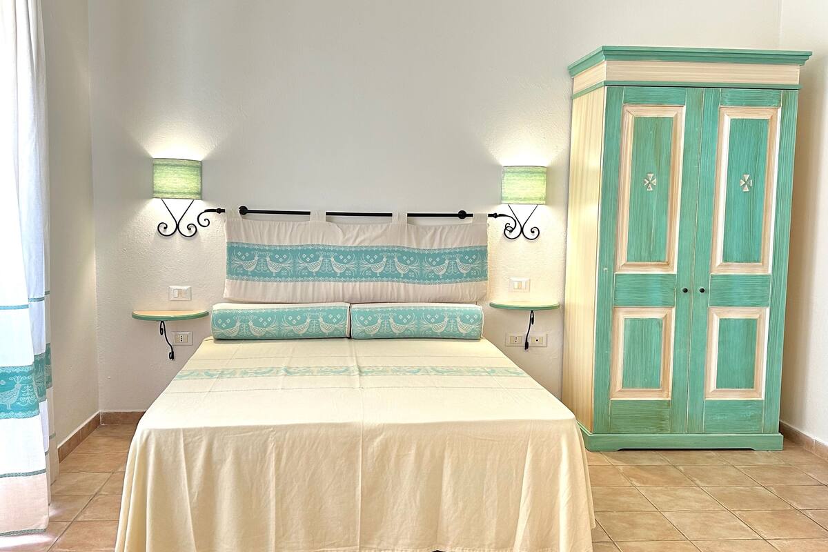 A bedroom with a bed, nightstands, a wardrobe, and wall-mounted lamps.