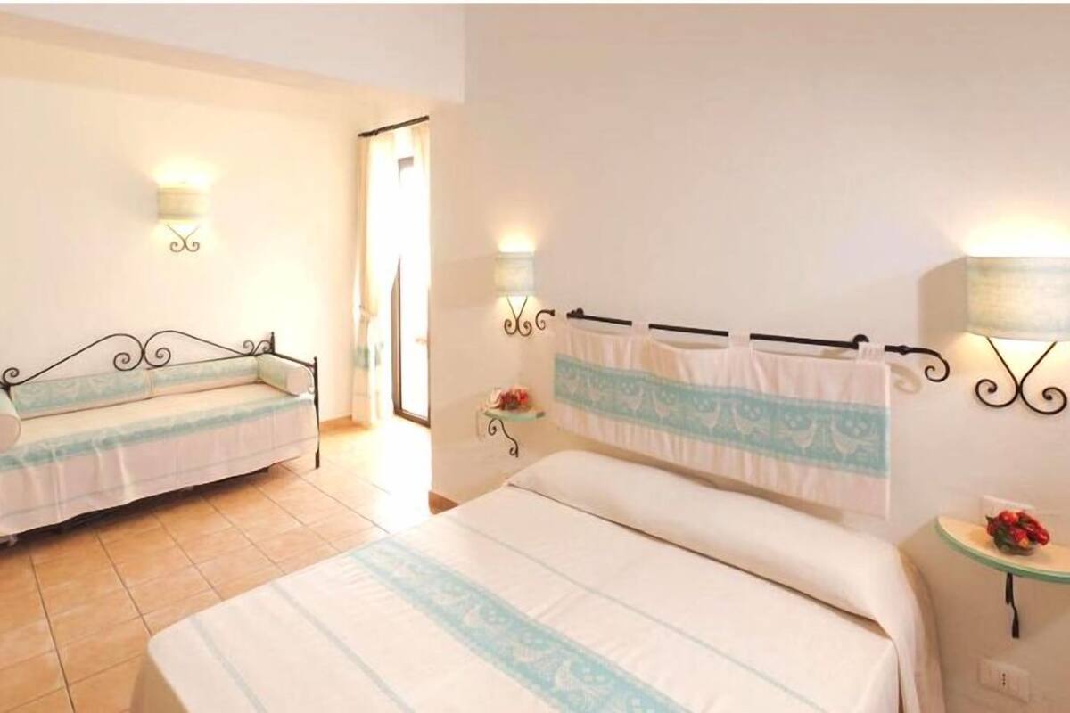 A bedroom with two beds, a bedside table with a lamp, and a small table with a fruit bowl.