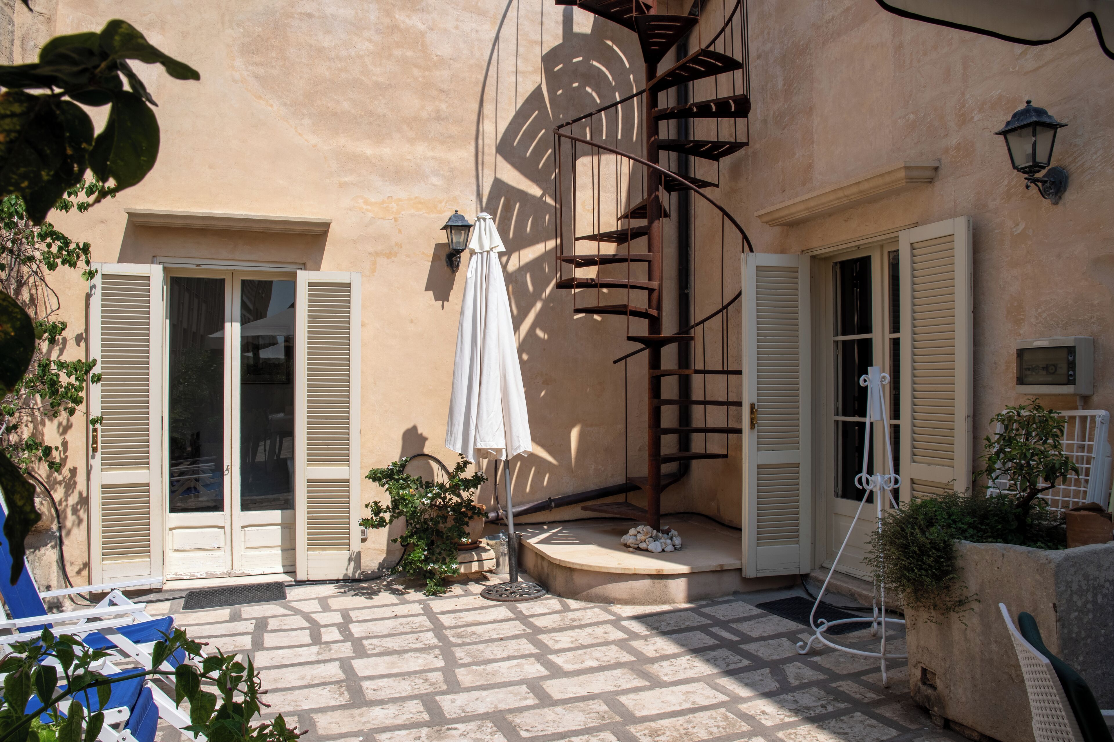 A courtyard with a spiral staircase, a potted plant, and a white umbrella.