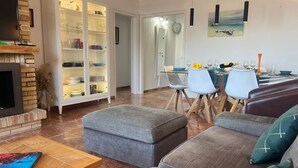 A modern living room with a fireplace, a dining area with a table set for four, and a kitchen area with a cabinet. - Roses - Los Sauces - Apart 3 rooms (Rosas / Roses)