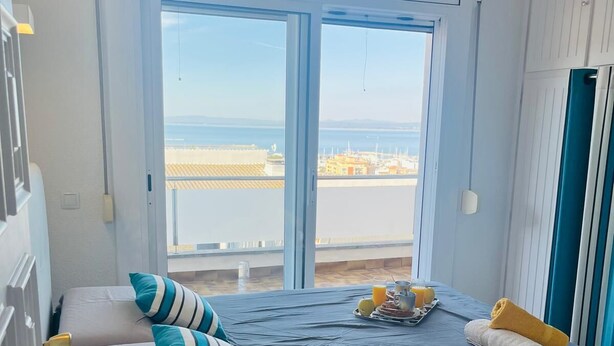 A bedroom with a large window, a bed with blue and white striped pillows, and a breakfast tray on the bed. - Roses - Los Sauces - Apart 3 rooms (Rosas / Roses)