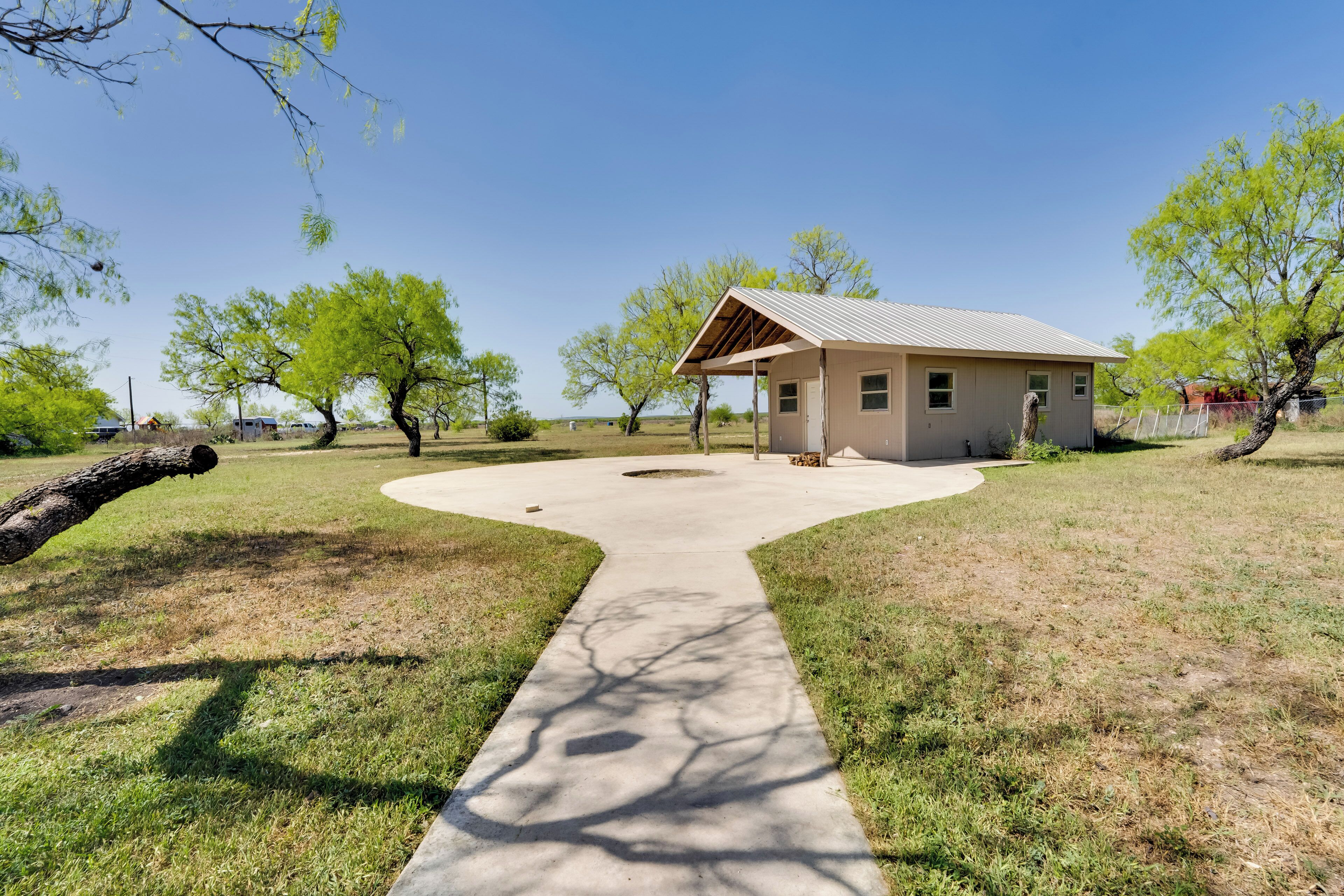 A small building with a covered patio, surrounded by grass and trees.