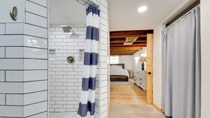 A bathroom with white tiled walls, a shower with a striped curtain, and a wooden ceiling.