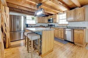 Una cocina con armarios de madera, electrodomésticos de acero inoxidable, una isla central con taburetes de bar y una lámpara colgante.