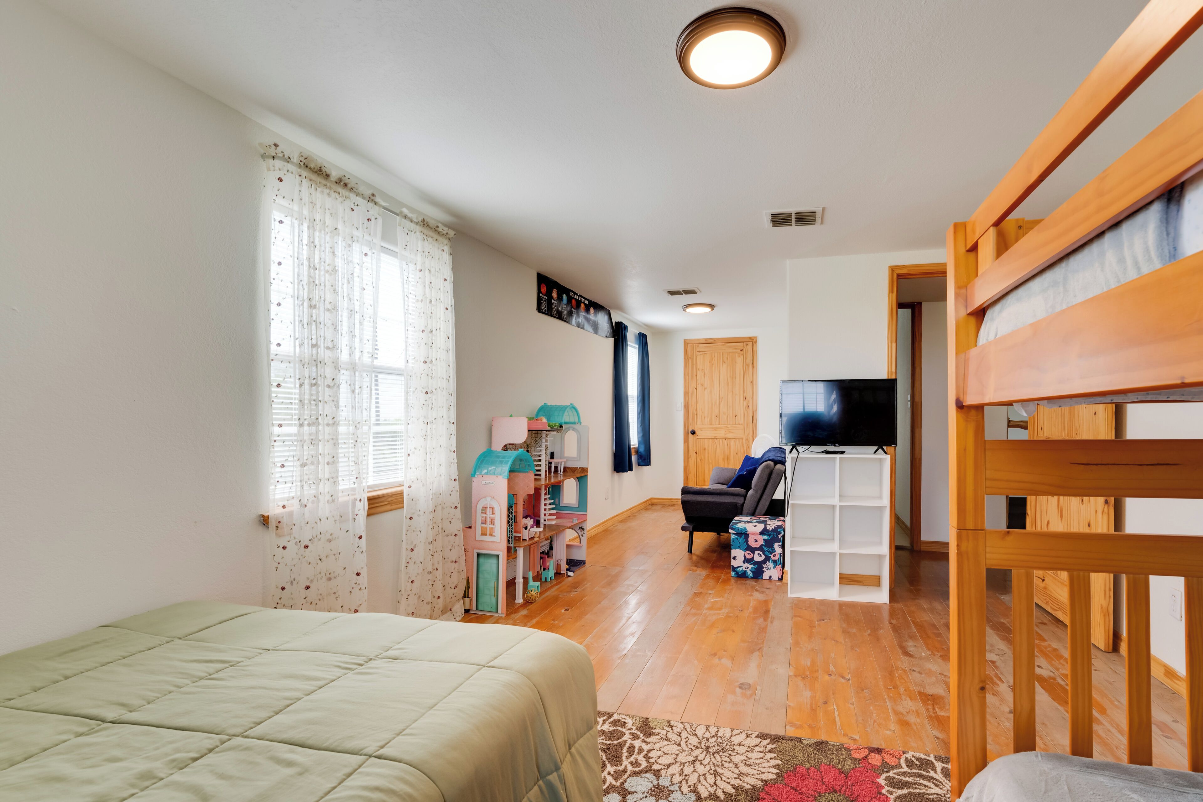 Ein Zimmer mit Etagenbett, Fernseher, Spielbereich mit Spielzeug und Holzboden.