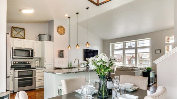 Cocina moderna con armarios blancos, horno empotrado y microondas. Hay una zona de comedor con una mesa para cuatro, sillas y un florero con flores.