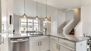Una cocina moderna con armarios blancos, encimera de granito e iluminación colgante.