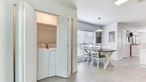 Een moderne keuken met witte kasten, een eethoek met een tafel en stoelen, en een wasruimte met een wasmachine en droger.